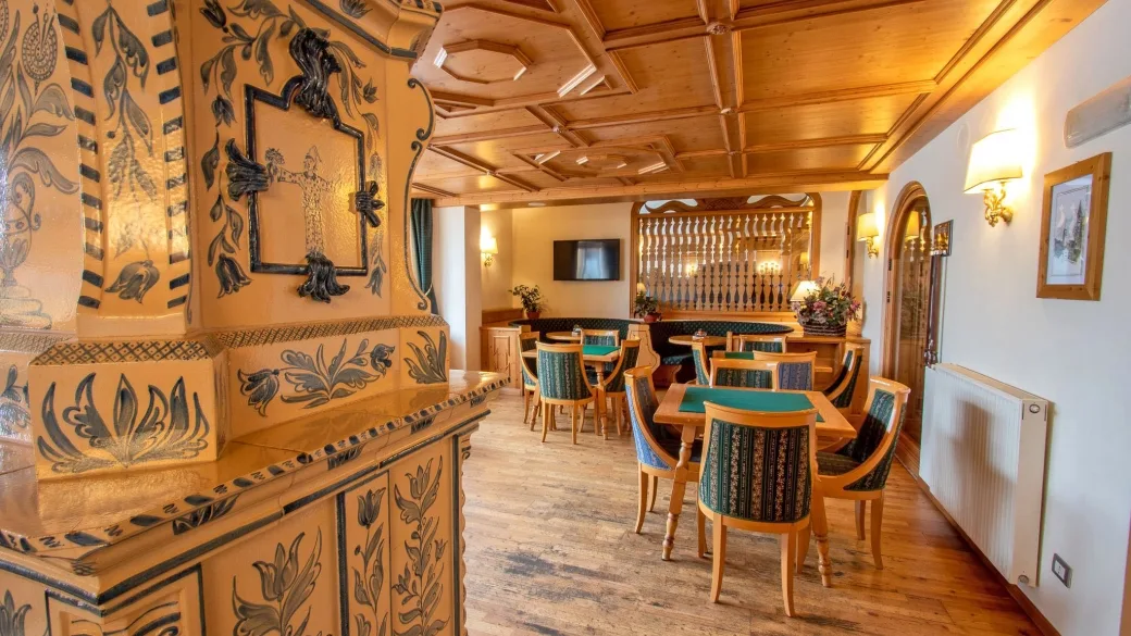 Sala con stufa in ceramica decorata, tavoli da gioco e soffitto in legno