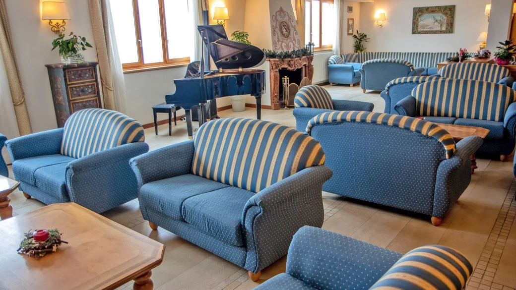 Salone lounge con divani blu a righe, pianoforte a coda e camino