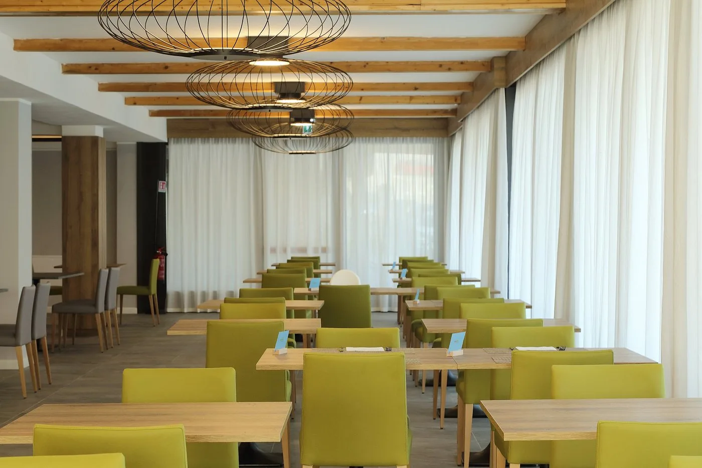 Sala da pranzo con sedie verdi, lampadari di design e grandi tende bianche