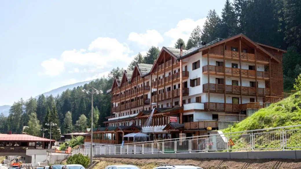 Esterno dell'hotel in estate con montagne boscose e parcheggio