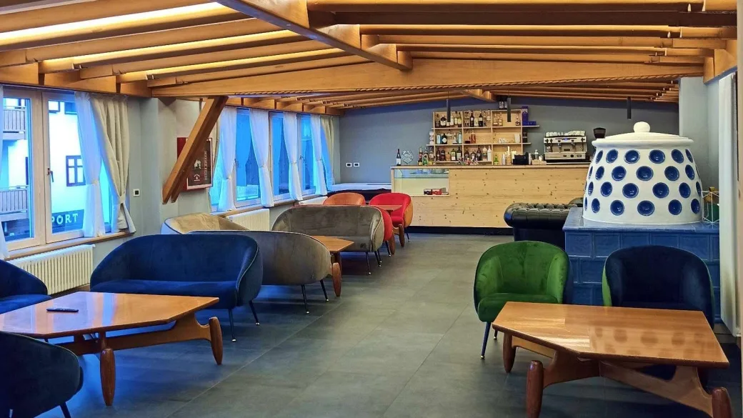 Area lounge bar con poltrone colorate, travi in legno e stufa in ceramica tradizionale
