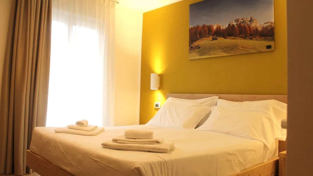 Camera accogliente con parete gialla, letto matrimoniale e asciugamani pronti