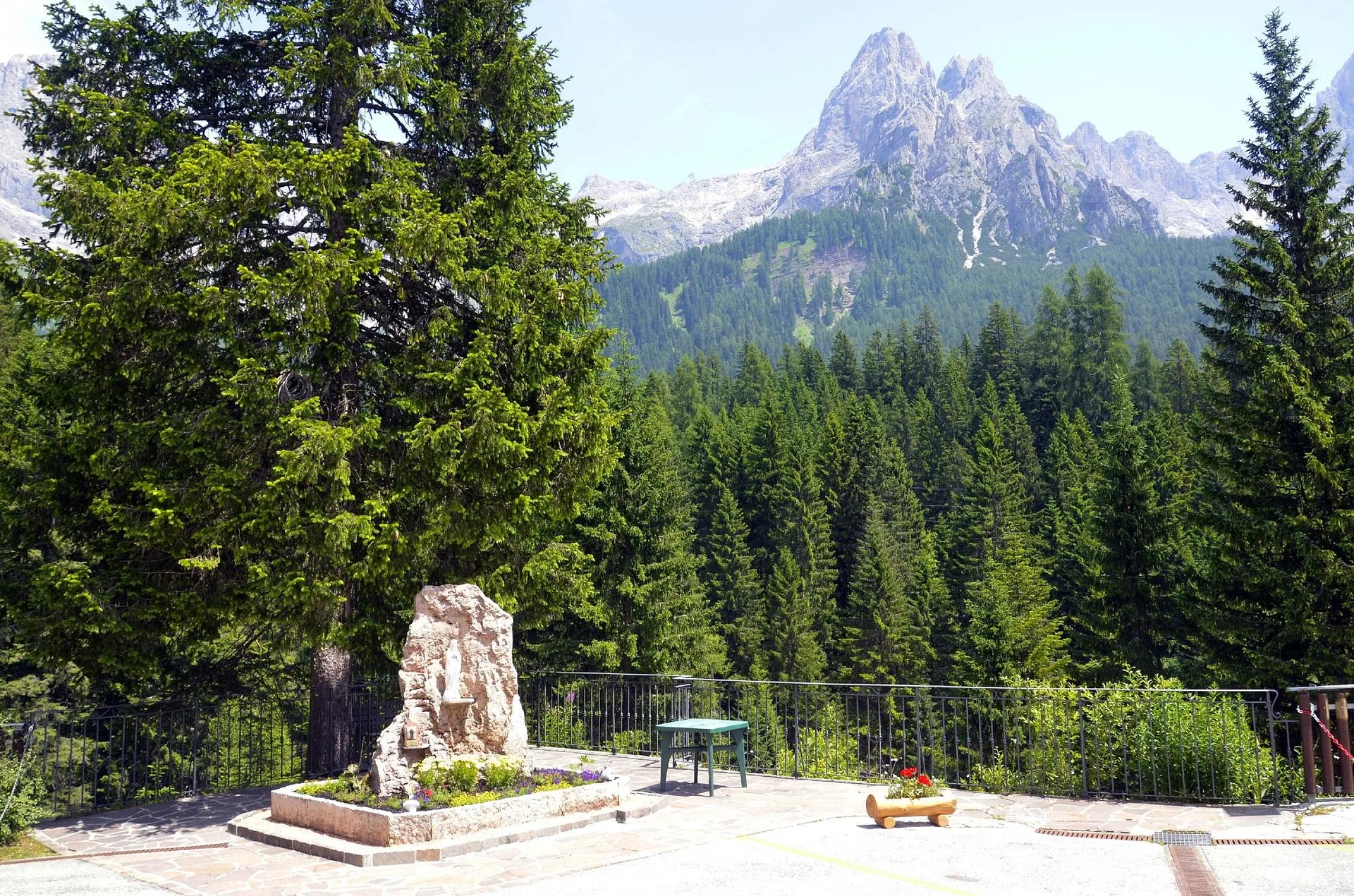 Area panoramica con aiuola fiorita, tavolo e vista sulle Dolomiti e boschi di conifere
