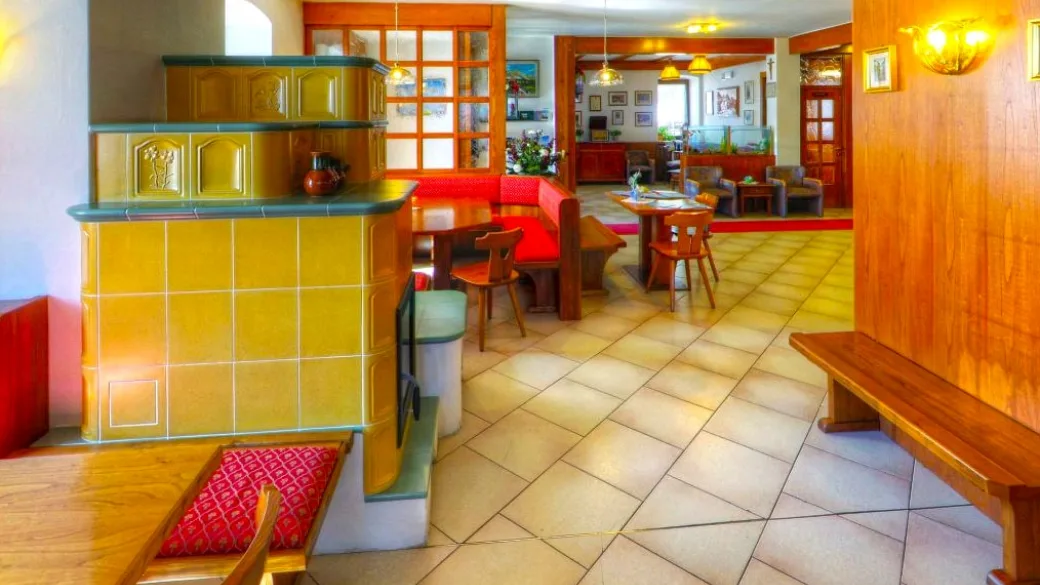 Area comune con stufa in maiolica gialla, panche in legno e zona soggiorno