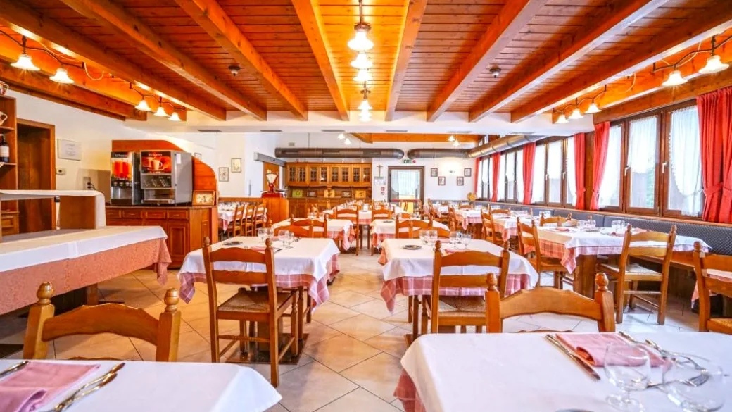 Sala da pranzo con travi in legno, tavoli con tovaglie rosa e tende rosse