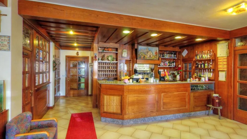 Reception e bar dell'hotel con arredi in legno, tappeto rosso e poltrona
