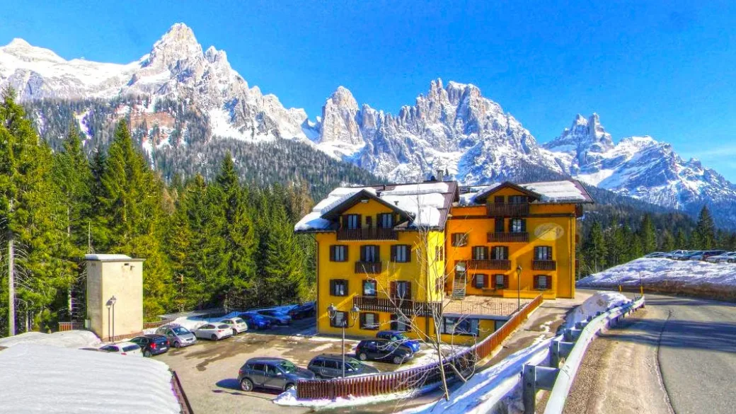 Hotel giallo con parcheggio in inverno e spettacolare panorama delle Pale di San Martino innevate