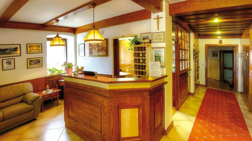 Reception in legno dell'hotel con divano, quadri alle pareti e corridoio con tappeto rosso