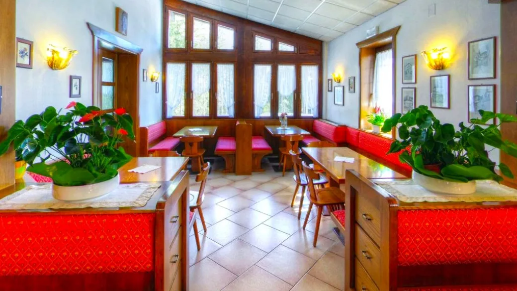 Sala con sedute rosse, tavoli in legno, piante verdi e ampie finestre
