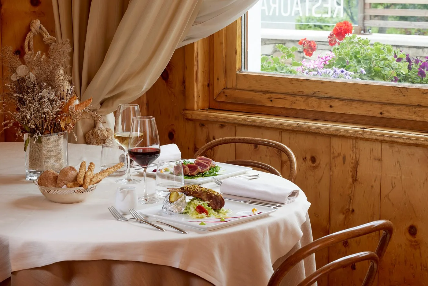 Tavolo apparecchiato accanto alla finestra con vista su fiori e piatti gourmet