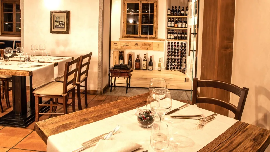 Sala ristorante con tavoli apparecchiati e cantina di vini a vista