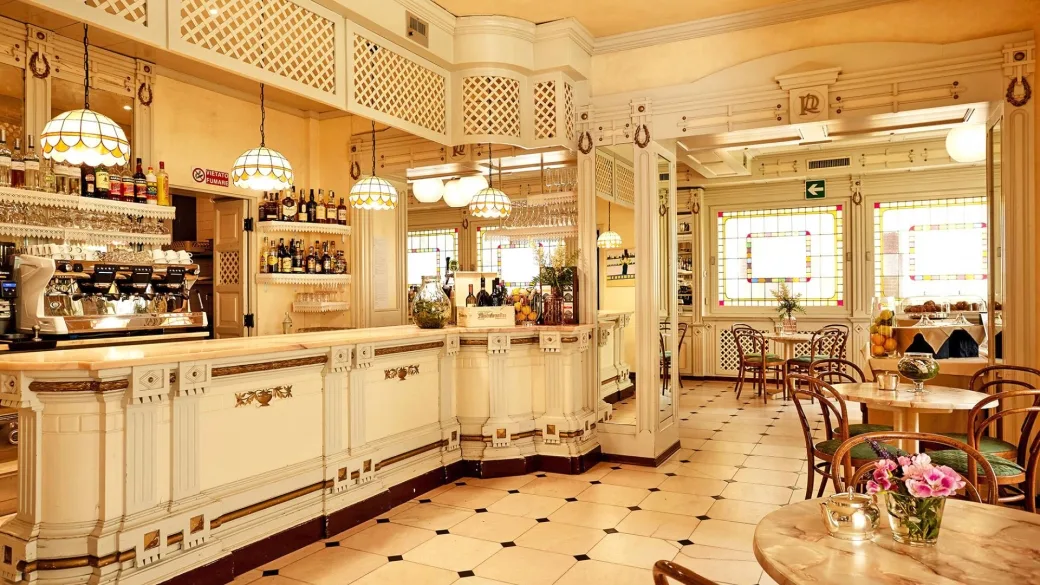 Bar interno in stile classico con bancone decorato e tavolini in marmo
