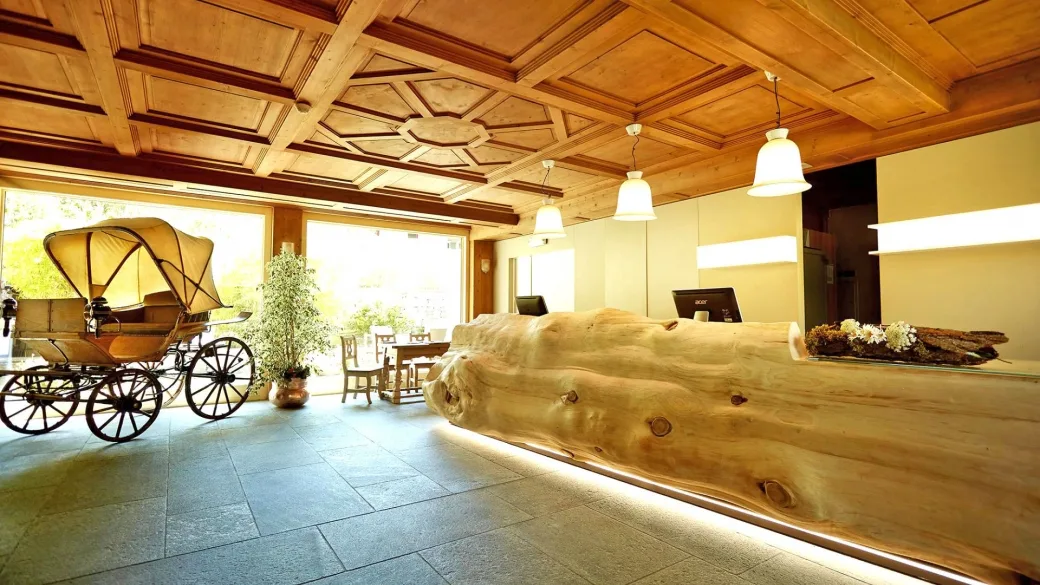 Reception dell'hotel con soffitto in legno, bancone in tronco e carrozza d'epoca