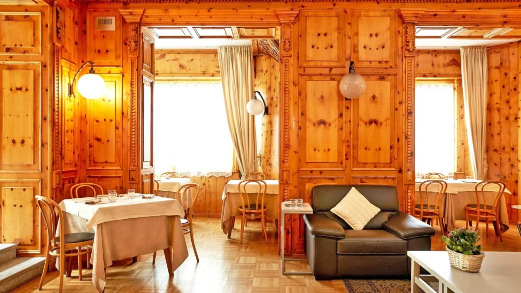 Sala da pranzo rivestita in legno di cirmolo con tavoli e poltrona