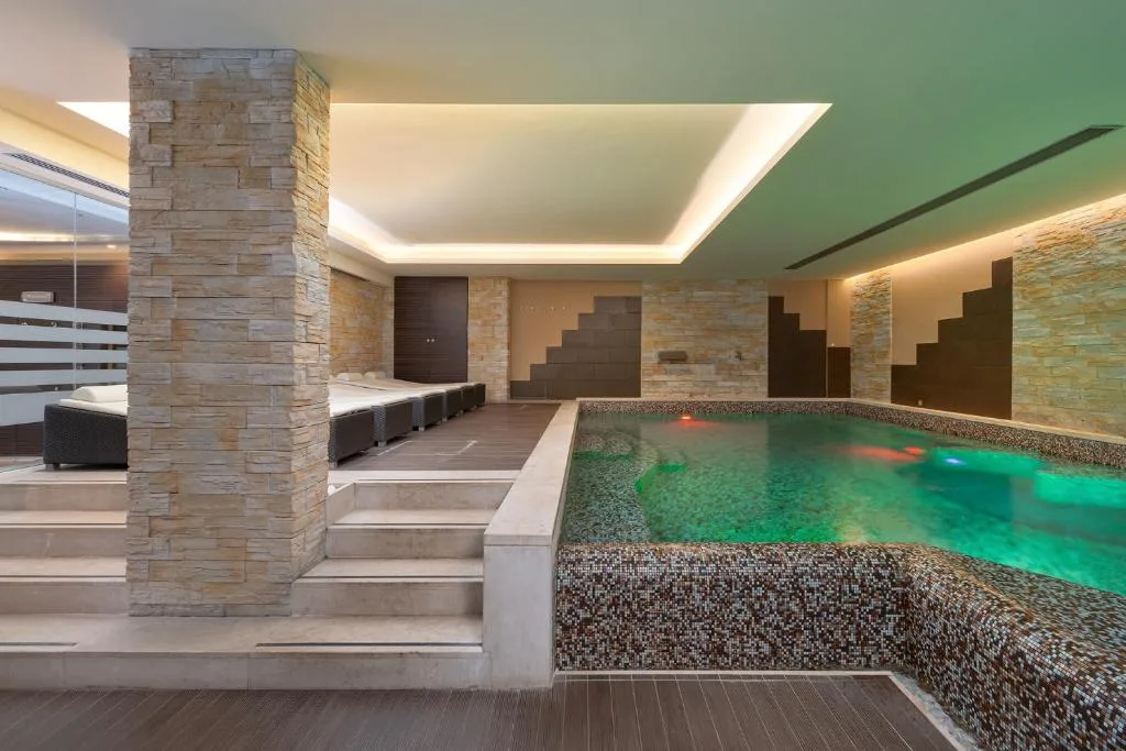 Area piscina interna con lettini, scale in pietra e illuminazione soffusa