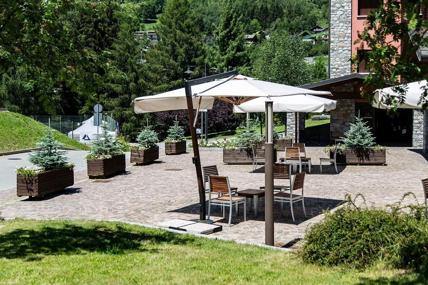 Terrazza esterna dell'hotel con ombrellone, tavoli e sedie immersa nel verde