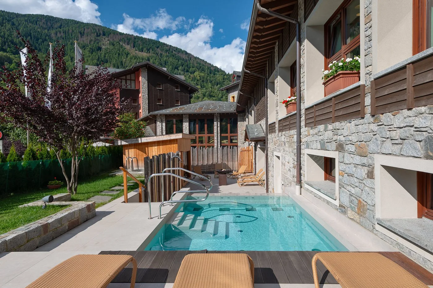 Piccola piscina esterna con lettini prendisole e sauna in legno in ambiente montano estivo