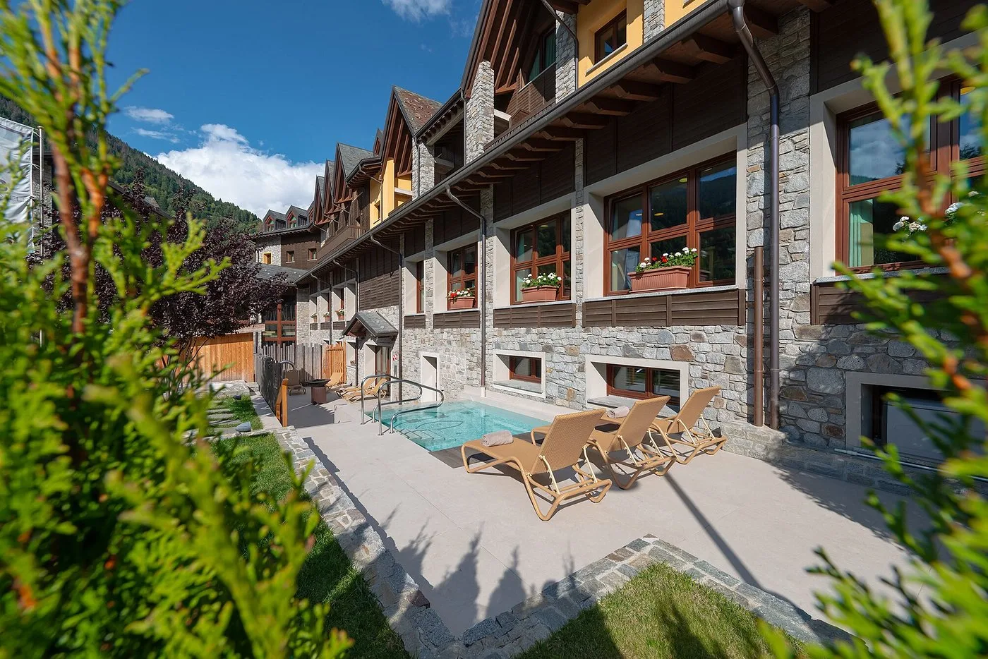 Area relax esterna con piscina idromassaggio, lettini e giardino in stile alpino