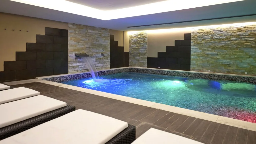 Piscina interna con cascata d'acqua, luci colorate e lettini relax