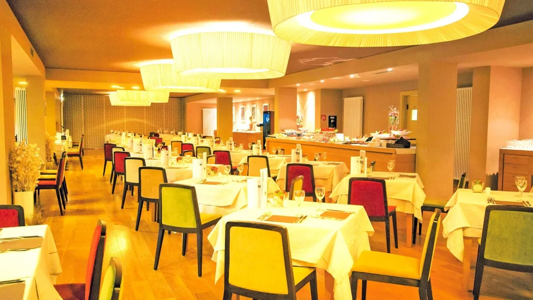 Sala ristorante dell'hotel con tavoli apparecchiati, sedie colorate e lampadari eleganti