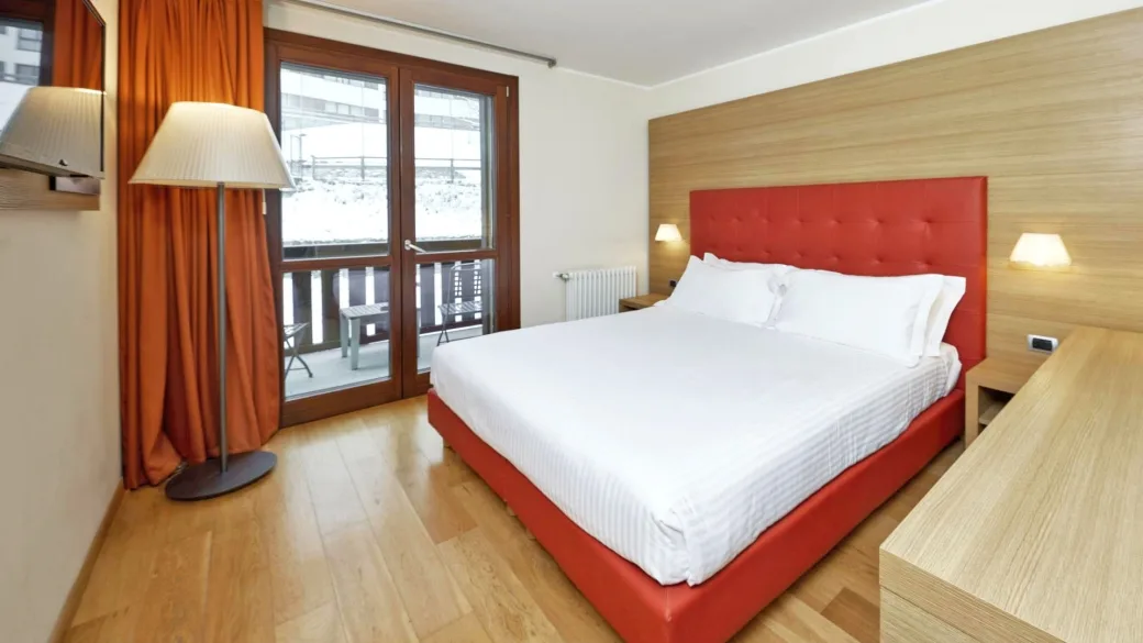 Camera matrimoniale con testiera rossa, parquet e balcone con vista invernale