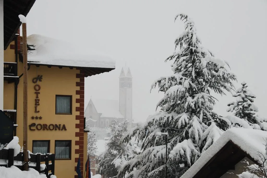 Hotel Corona sotto la neve con alberi innevati e campanile del paese sullo sfondo