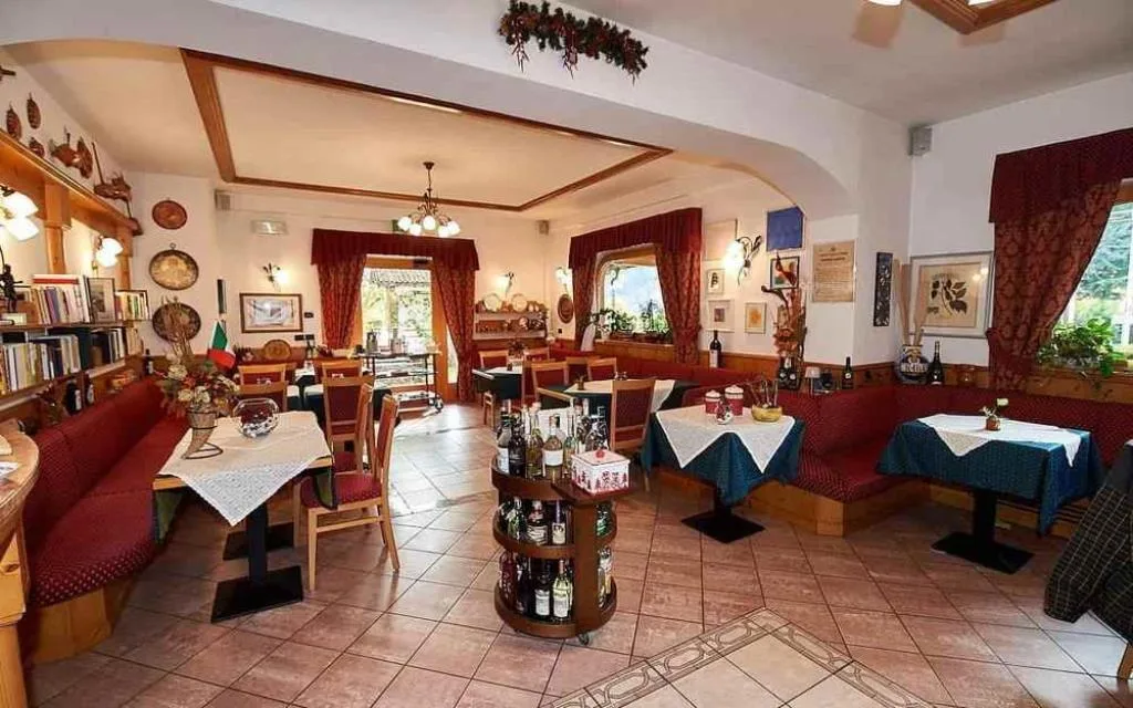 Sala ristorante rustica con panche rosse, tavoli in legno e oggetti tradizionali alle pareti