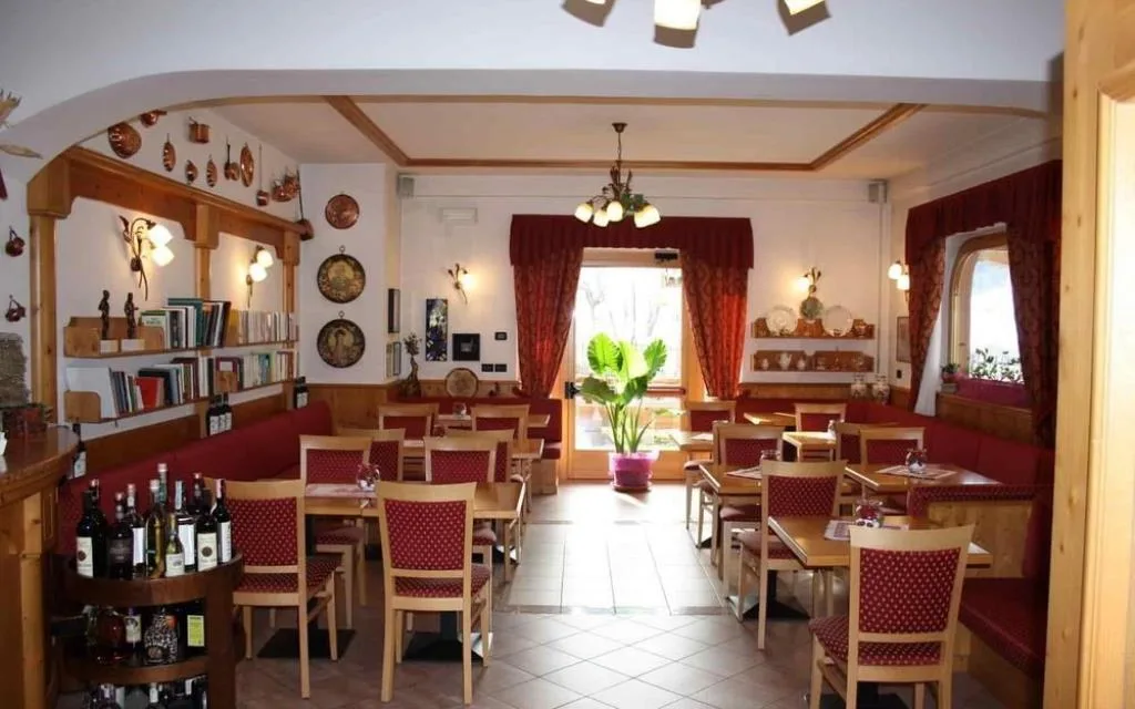 Sala ristorante rustica con tavoli, panche rosse e arredi tradizionali in legno