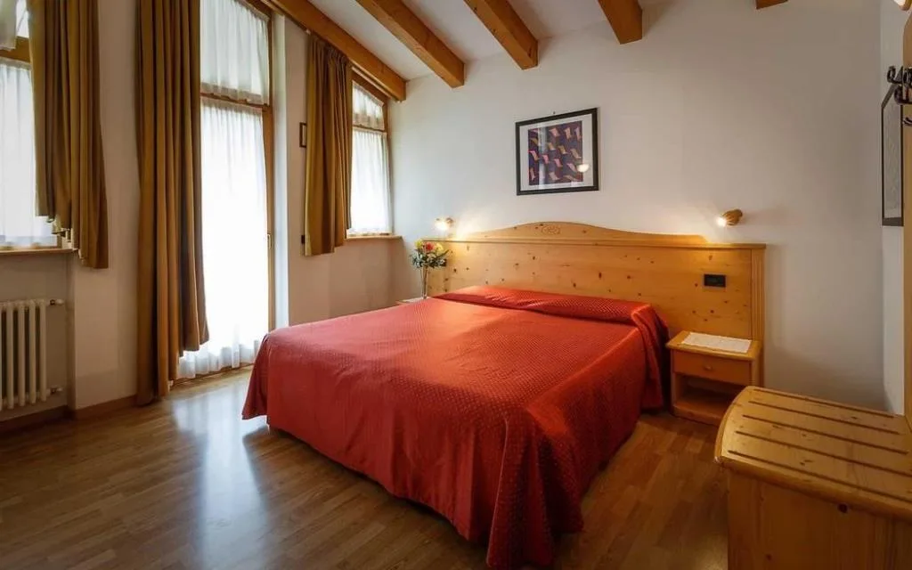 Camera matrimoniale con letto dal copriletto rosso, pareti chiare e travi in legno