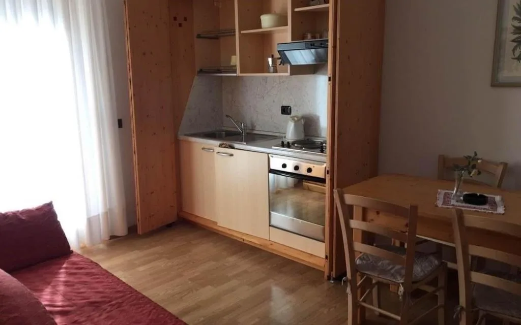 Monolocale con cucina compatta in legno, tavolo e divano letto