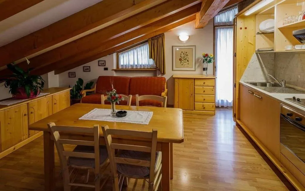 Soggiorno mansardato di un appartamento con travi in legno, tavolo, divano e angolo cottura