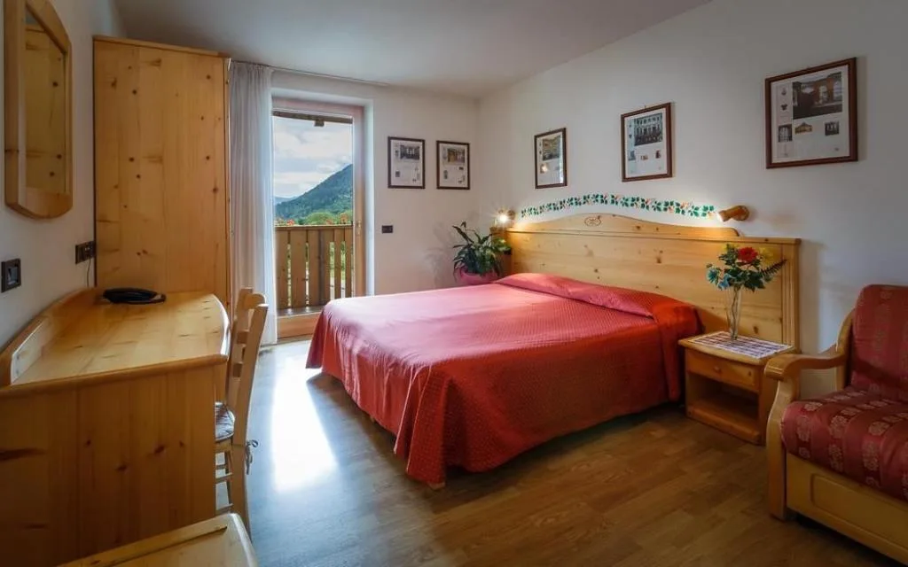 Camera matrimoniale luminosa con arredi in legno, poltrona e balcone con vista sui monti