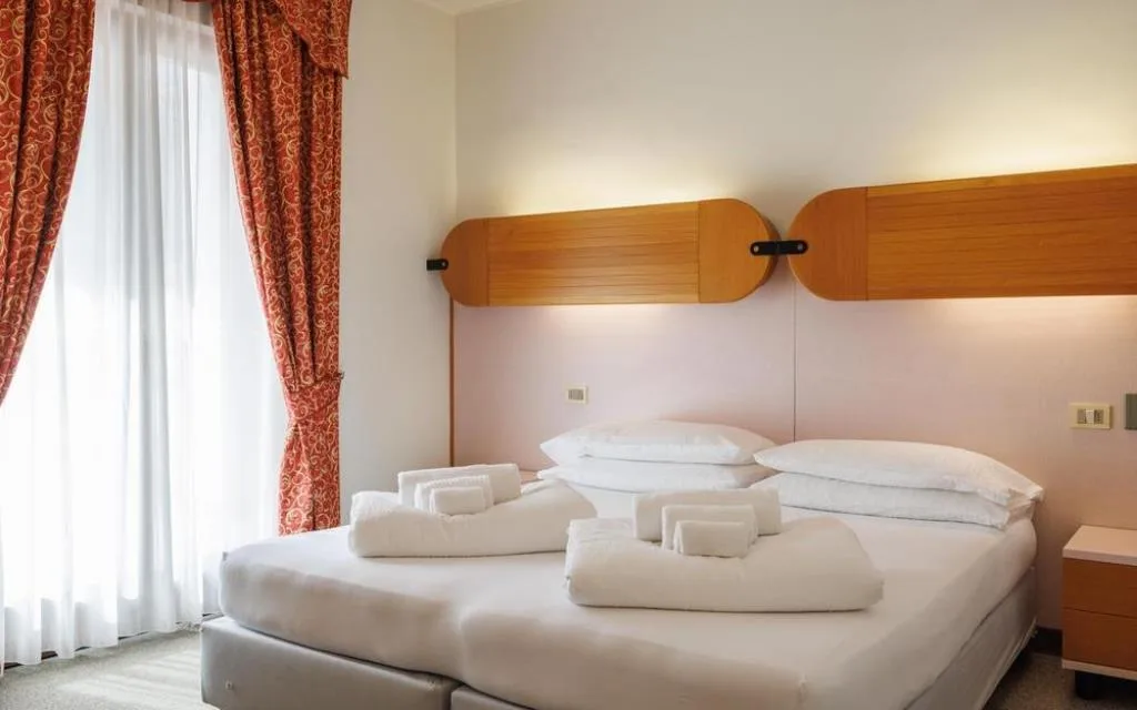 Camera matrimoniale con testiera in legno, tende rosse e asciugamani sul letto