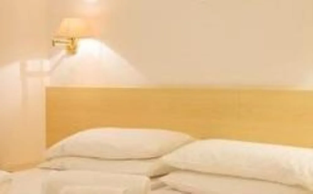Primo piano di un letto con testiera in legno chiaro e applique da parete