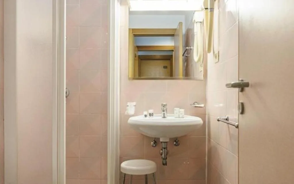 Bagno con piastrelle rosa, lavabo, specchio e sgabello bianco