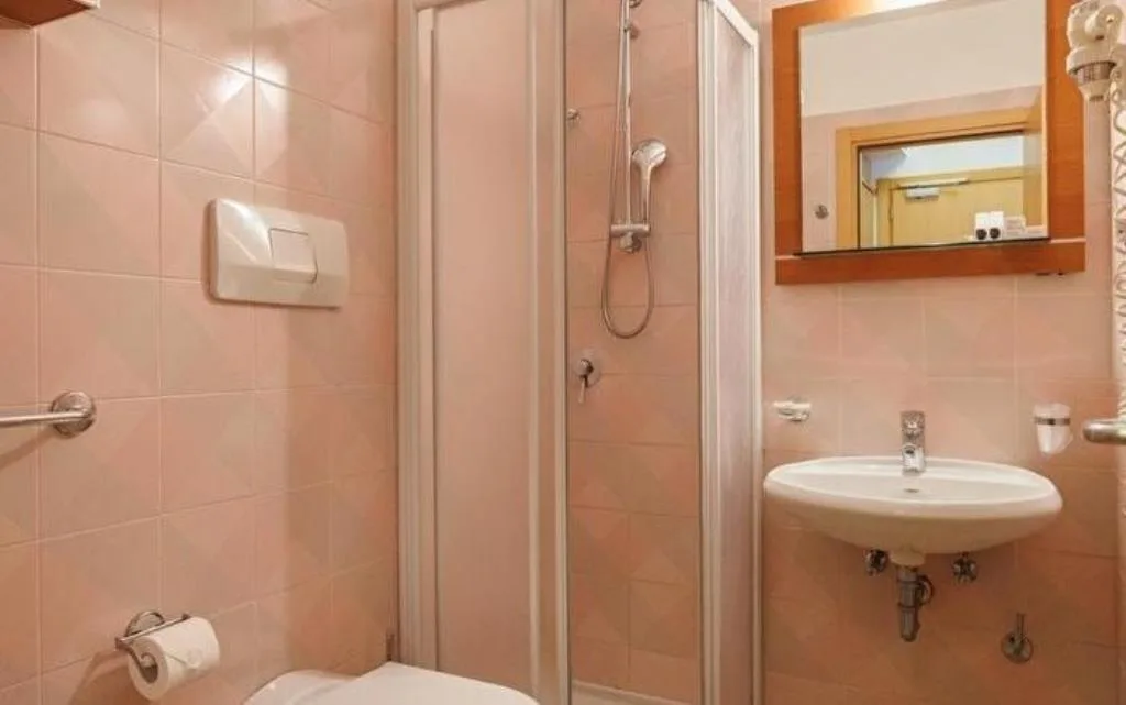 Bagno con piastrelle rosa, doccia, wc e lavabo a parete