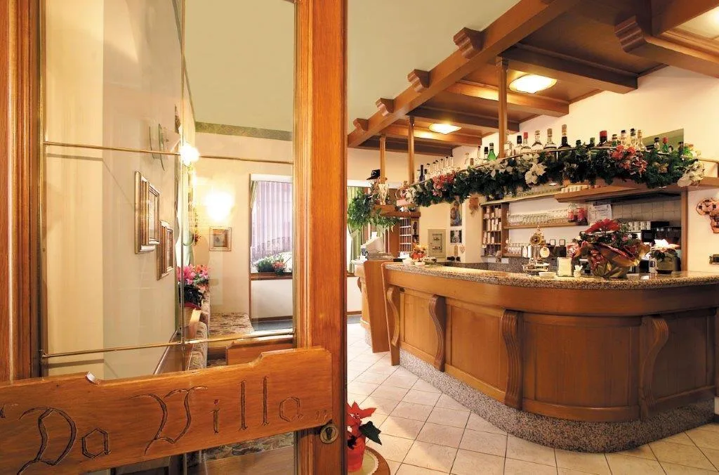 Vista del bar dell'hotel con bancone in legno, bottiglie e decorazioni floreali