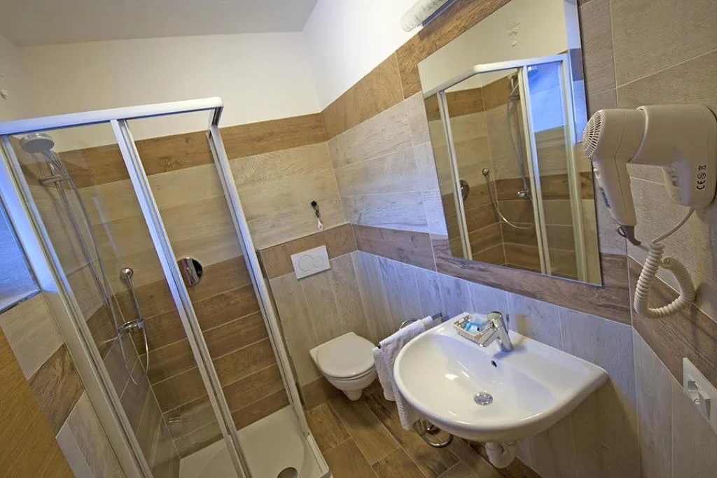 Bagno privato con doccia in vetro, lavabo, WC sospeso e piastrelle effetto legno