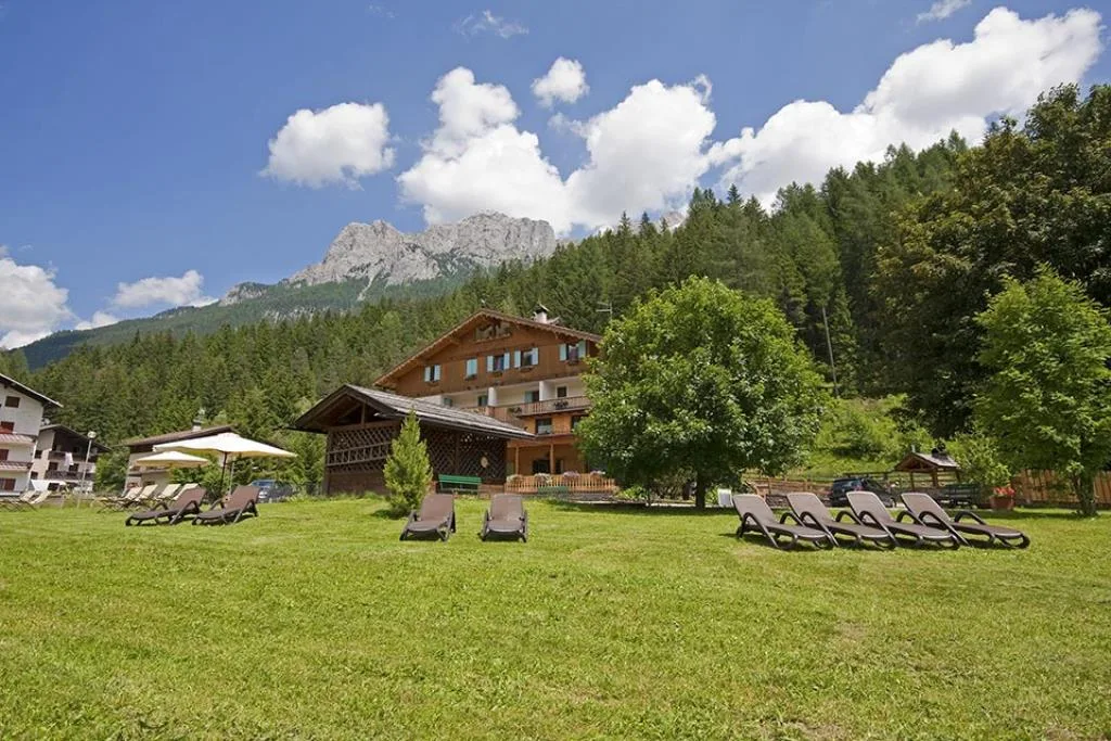 Prato verde con lettini e ombrelloni davanti all'hotel con montagne dolomitiche sullo sfondo in estate