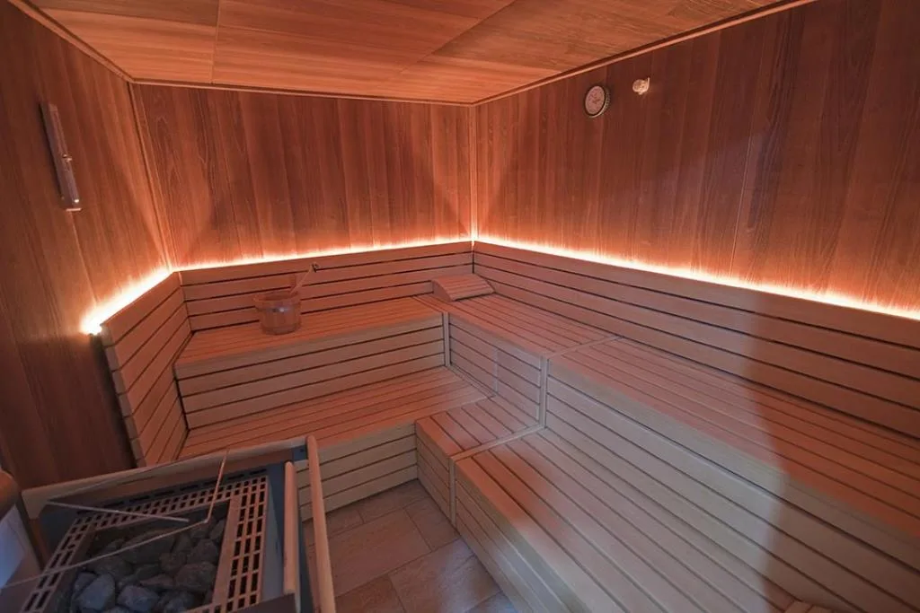 Sauna finlandese in legno con panche, stufa a pietre e illuminazione soffusa