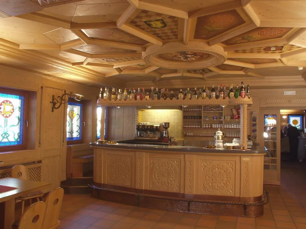 Bancone bar in legno intagliato con bottiglie esposte e soffitto decorato
