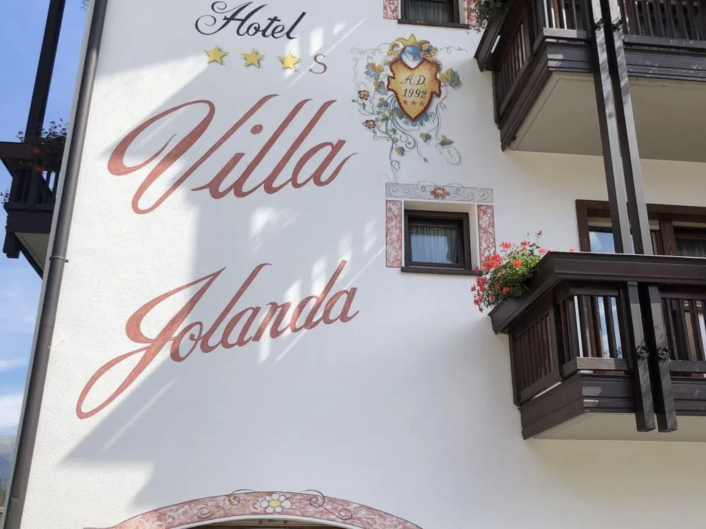 Insegna dipinta dell'Hotel Villa Jolanda sulla facciata con balconi fioriti
