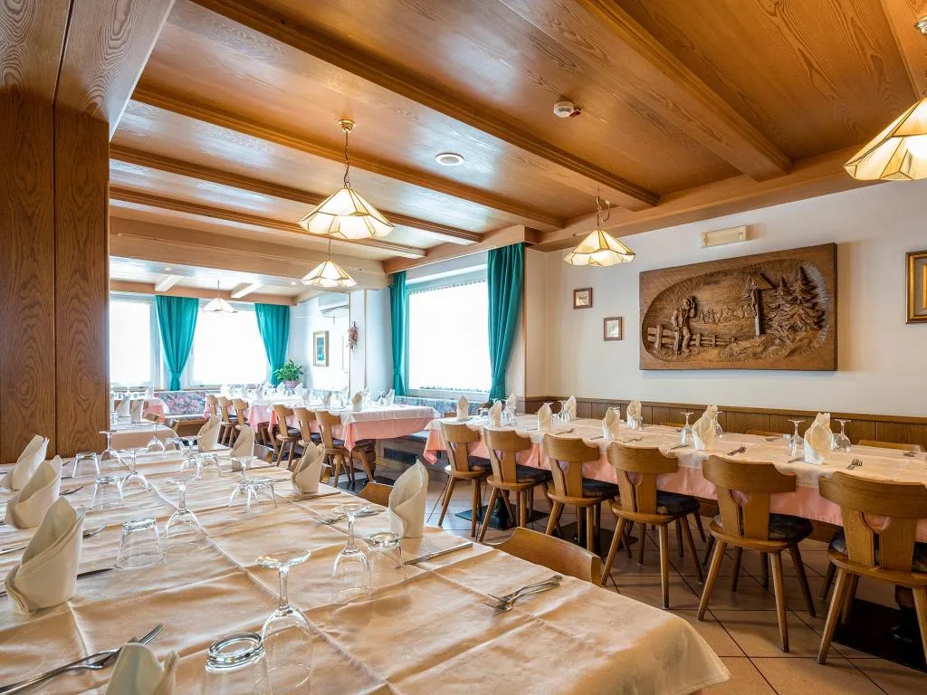 Sala ristorante con soffitto in legno, tavoli apparecchiati e tende verdi