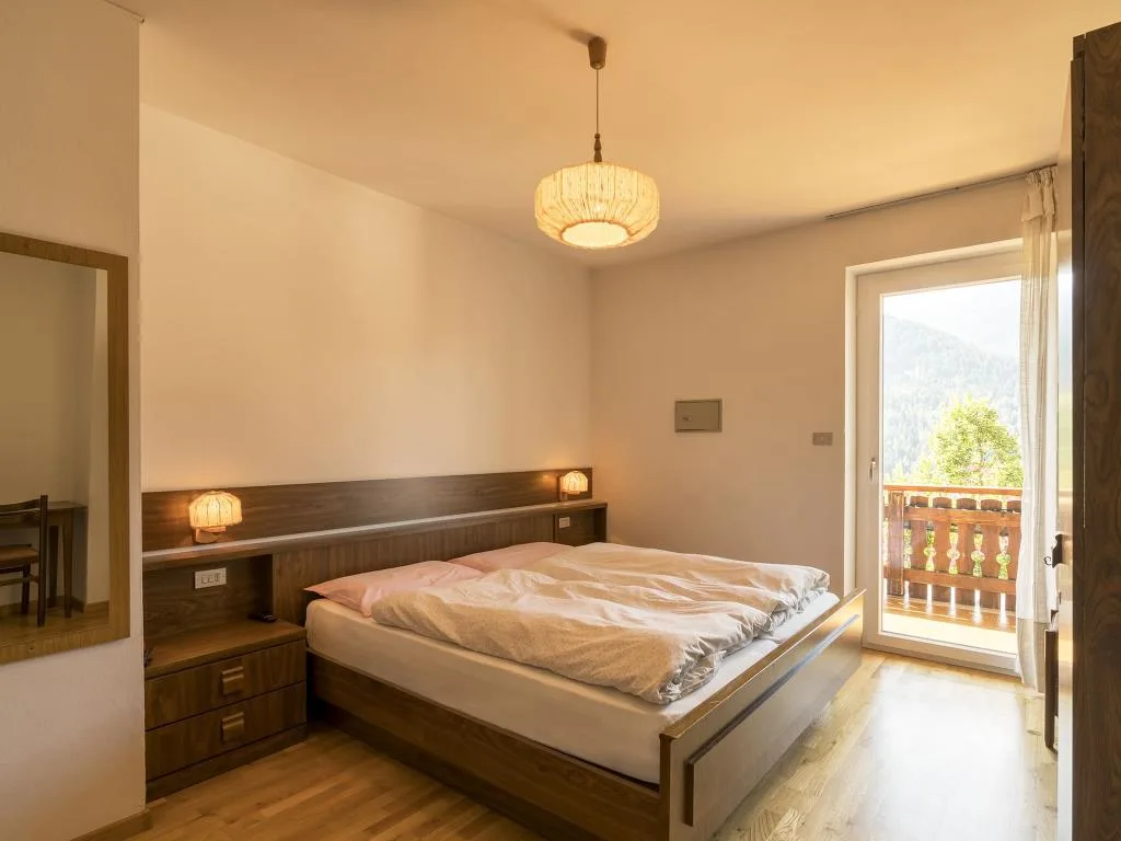 Camera da letto matrimoniale con arredi in legno, lampadario e porta finestra con vista sui monti