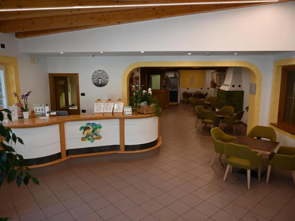 Reception dell'hotel con bancone curvo in legno e area lounge con poltrone verdi