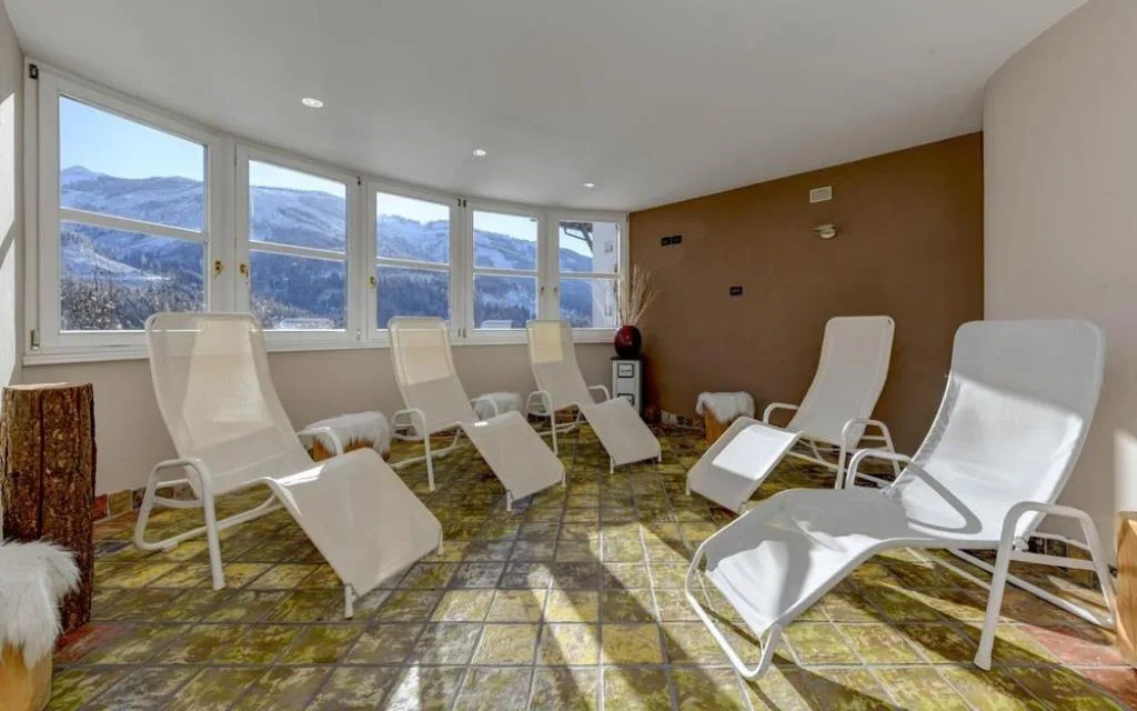 Zona relax della spa con lettini bianchi e ampie vetrate sui monti innevati