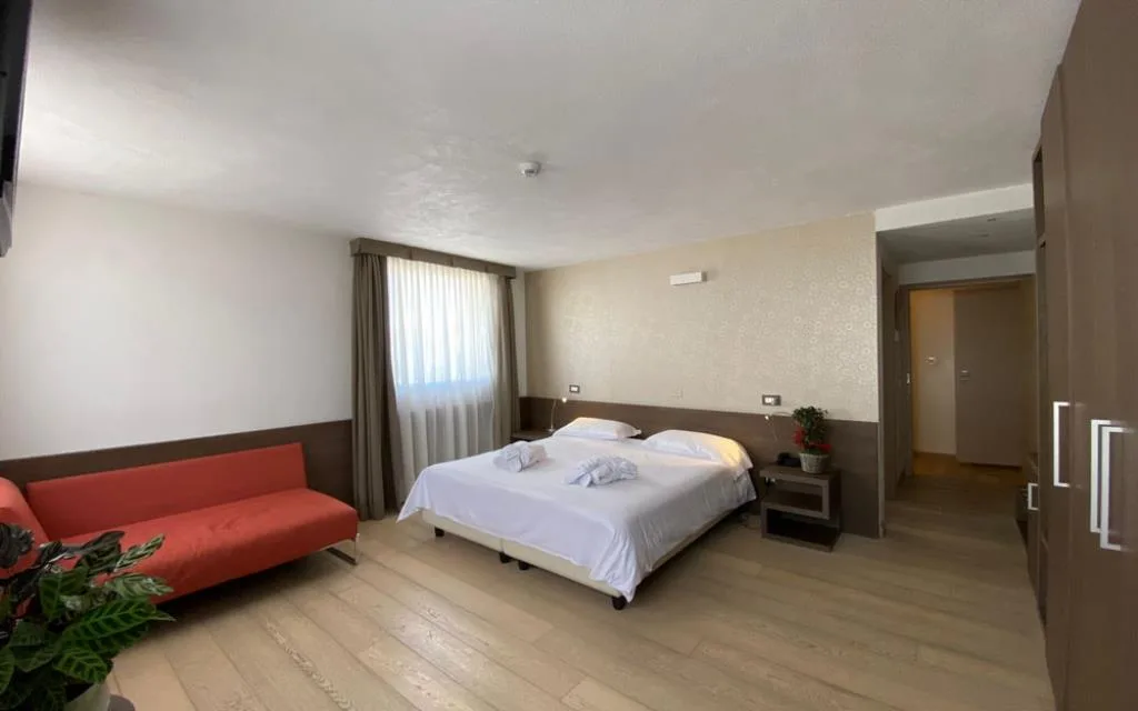 Ampia camera con letto matrimoniale, divano rosso e pavimento in parquet chiaro