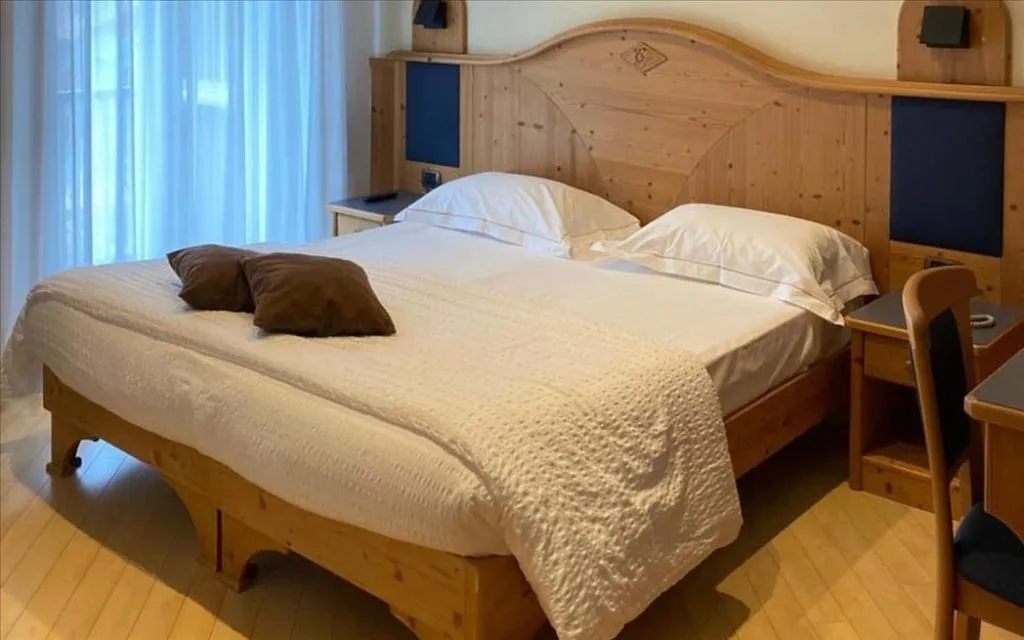 Camera matrimoniale con testiera in legno intagliato, cuscini marroni e tende bianche