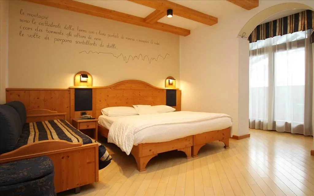 Camera spaziosa con letto in legno, divano, travi a vista e scritta decorativa a parete