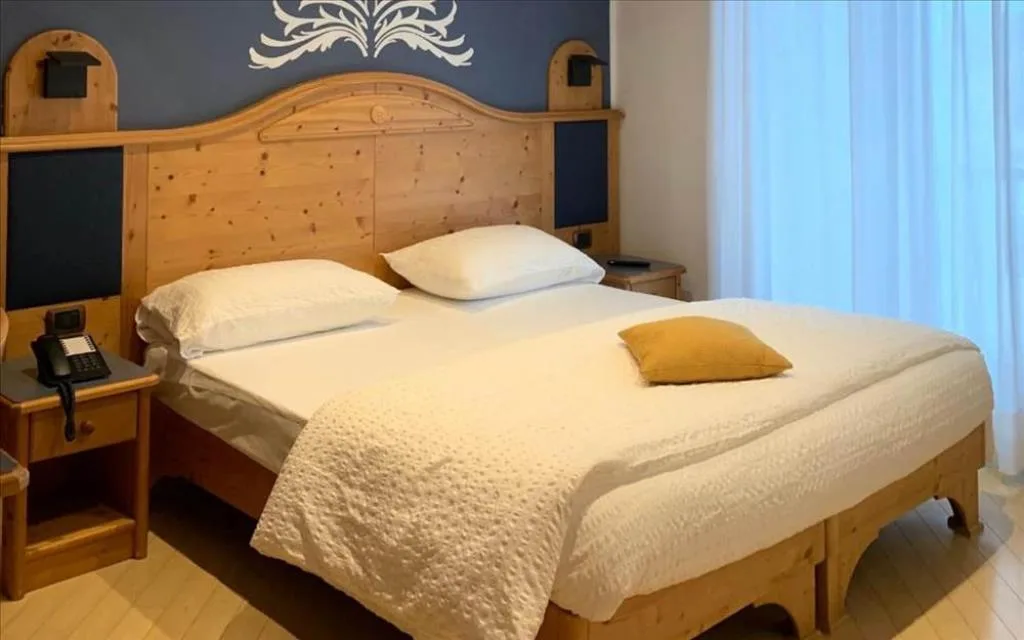 Camera con letto in legno chiaro, parete blu decorata e comodino con telefono